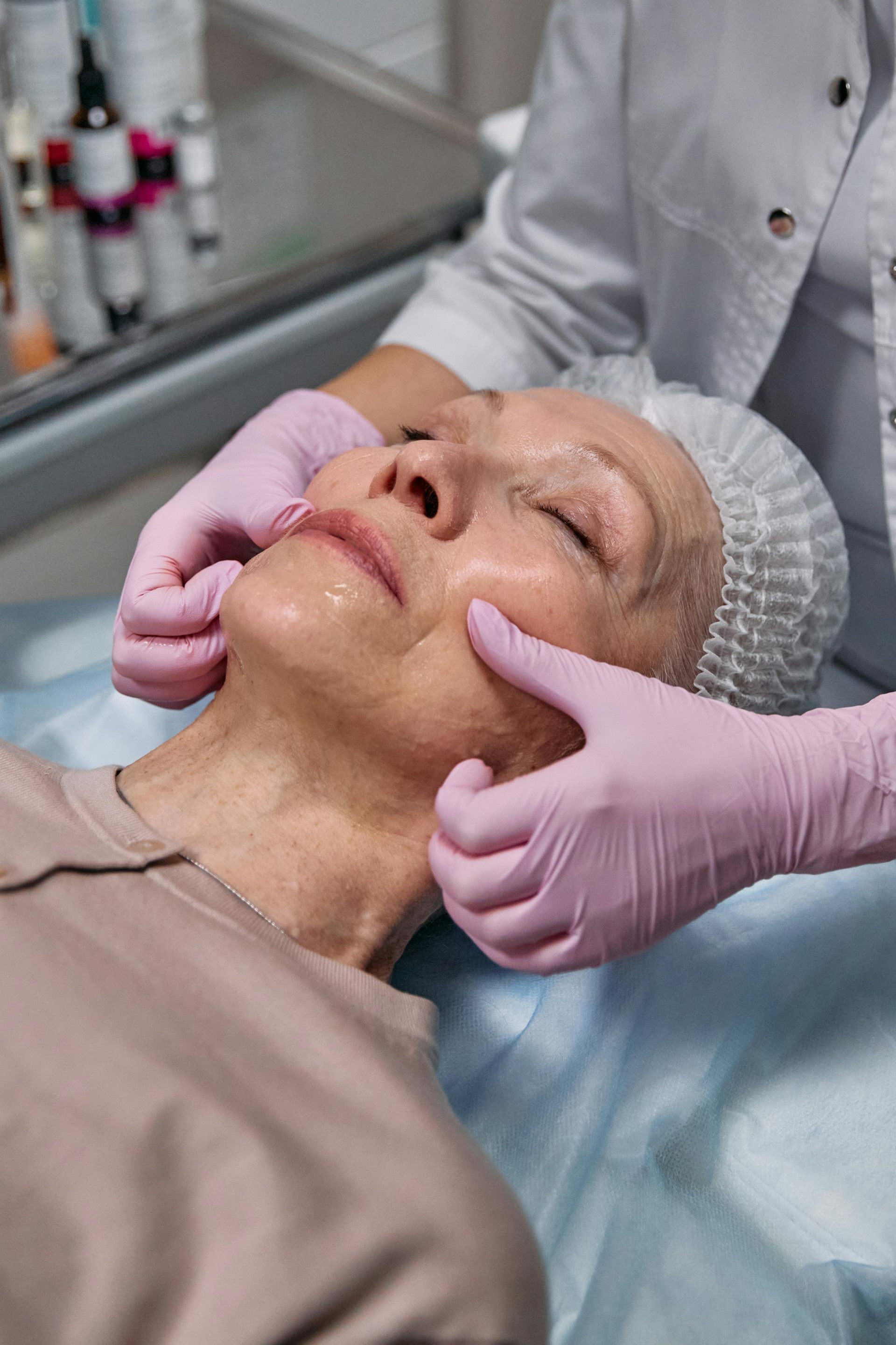 A senior woman receiving a relaxing facial massage in a professional clinic setting.