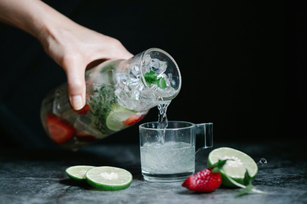 Close-up of a refreshing lime and strawberry infused drink being poured from a pitcher into a glass.